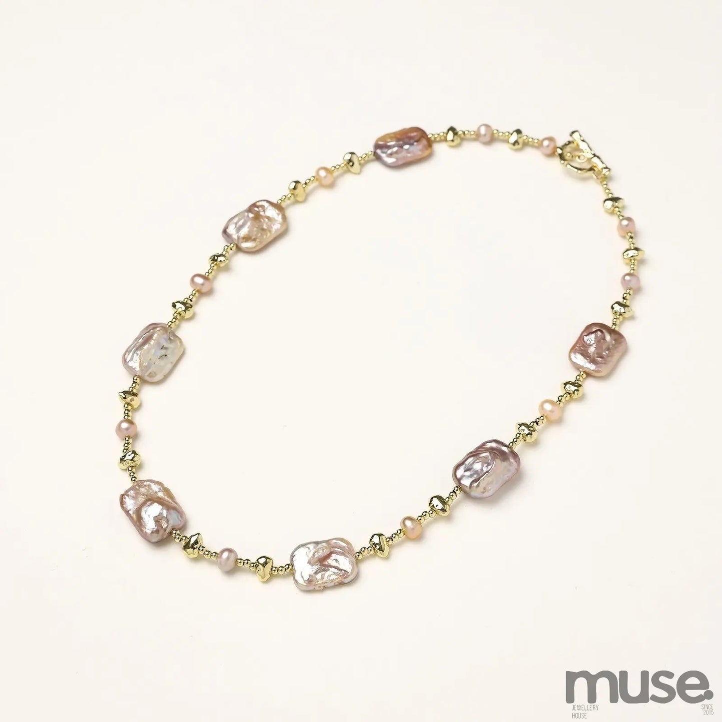 Long gold-plated necklace with iridescent baroque pearls and round freshwater pearls on cream background