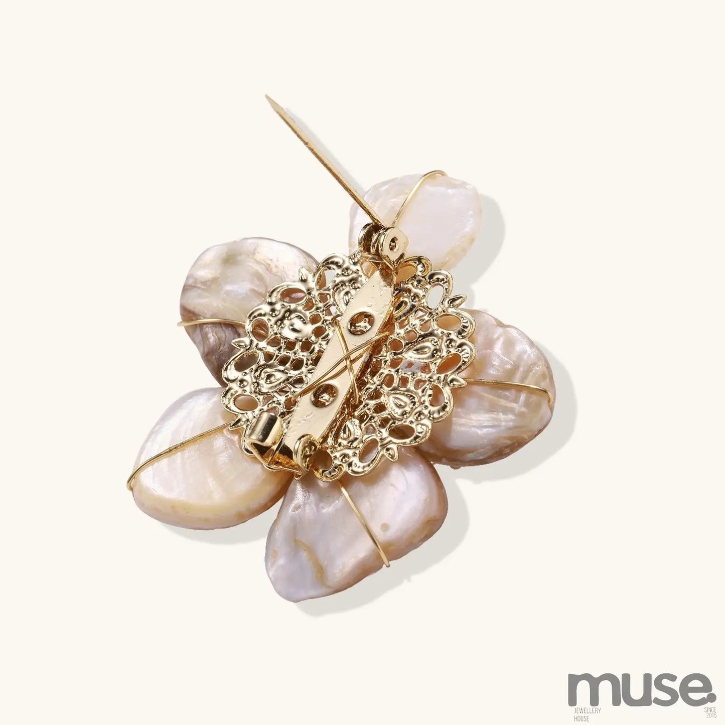 Elegant floral pin with peachy shell petals, gold radiating spokes, and white freshwater pearl center on cream background.