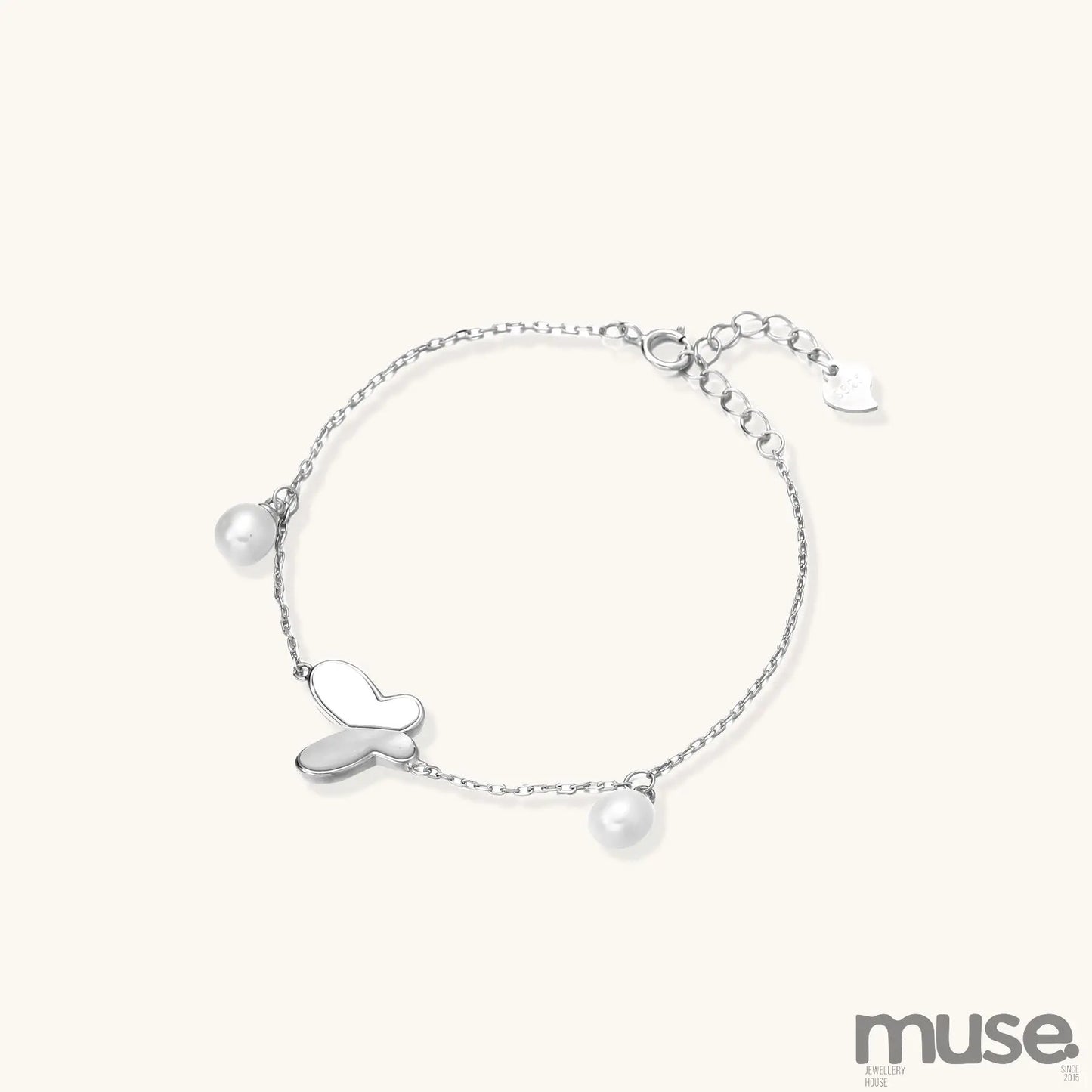 Dainty sterling silver chain bracelet with heart charm and freshwater pearl dangles on white background.