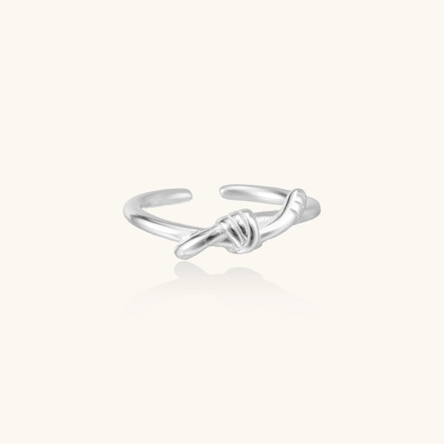 Delicate sterling silver ring with geometric knot design on white background, showcasing adjustable open band.