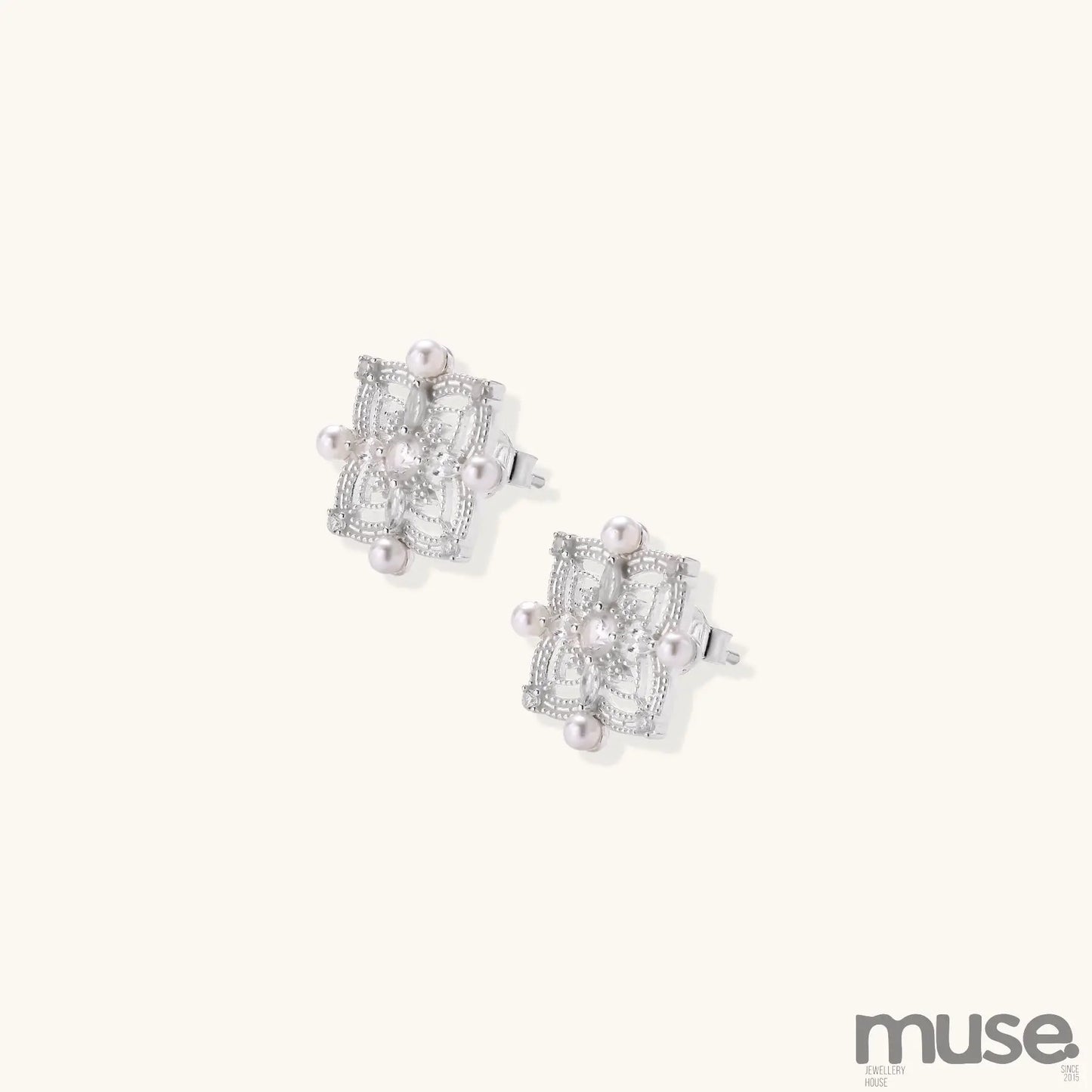 Detailed view of sterling silver stud earrings with geometric filigree design and small freshwater pearls on white background.