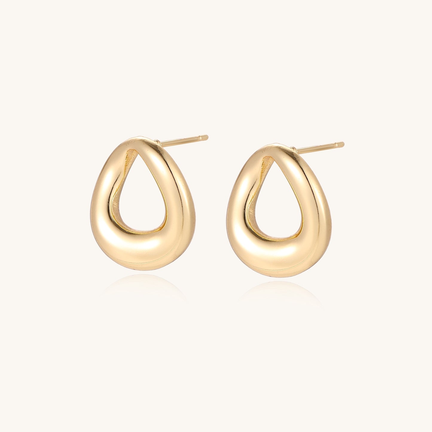 Pair of polished 18K gold-plated stainless steel oval loop stud earrings on cream background