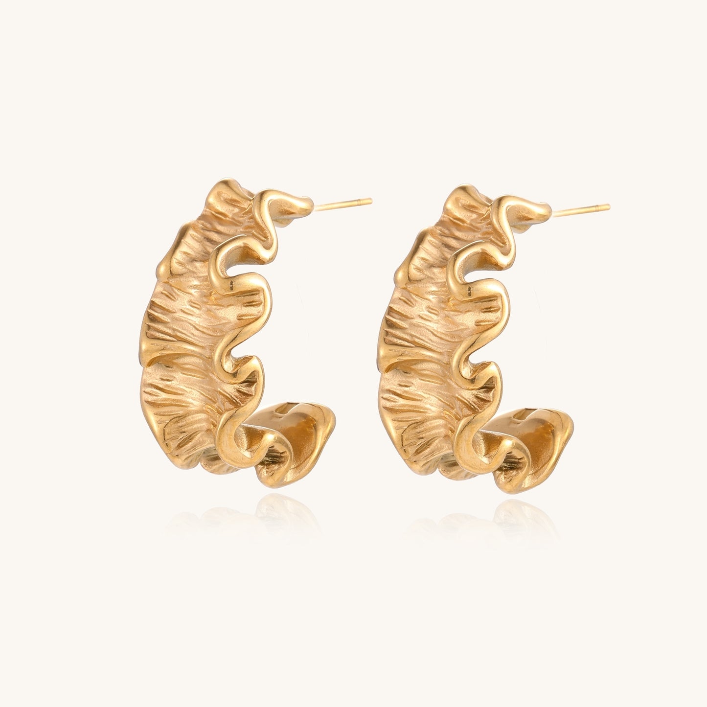 Textured gold-plated hoop earrings with wavy sculptural ridges displayed against a neutral background.