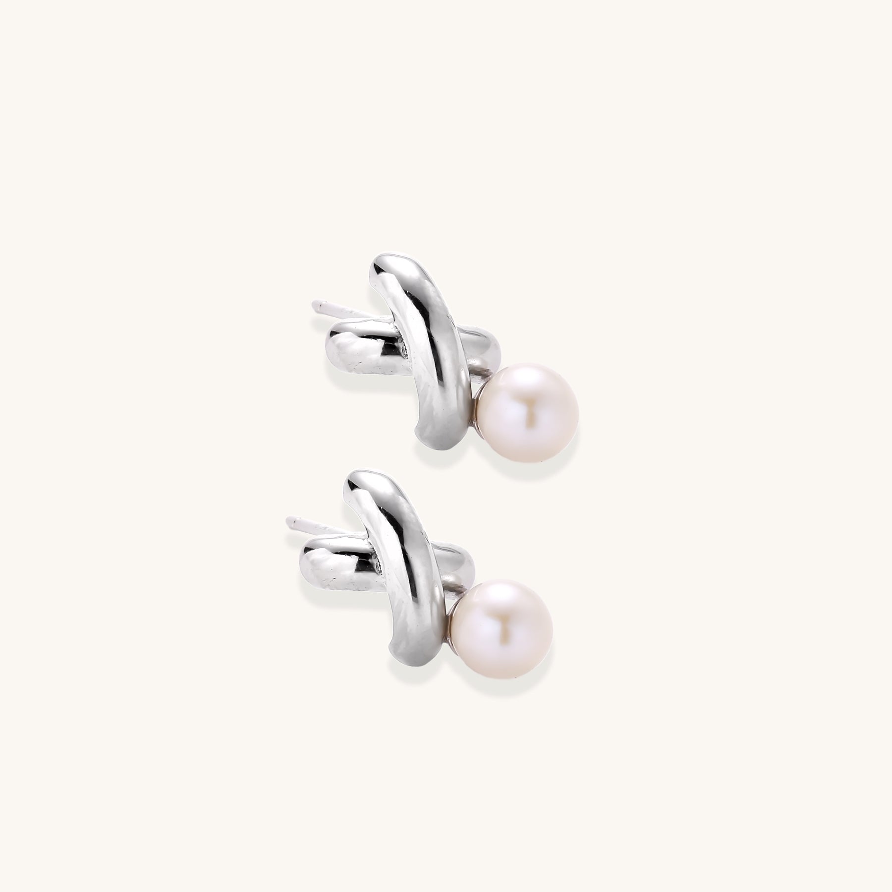 Sterling silver twisted stud earrings with round freshwater pearls on cream background, showing polished finish