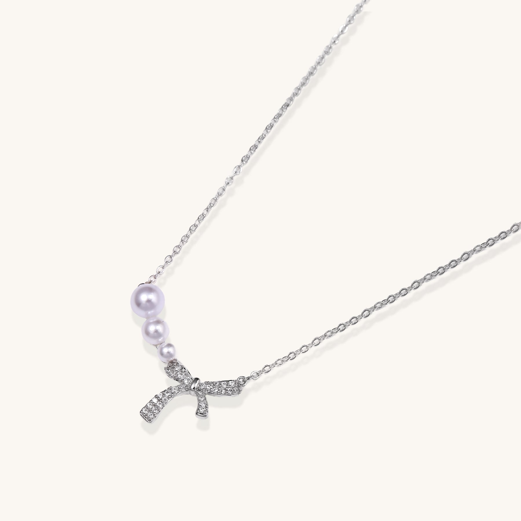 Dainty 14K gold plated necklace with freshwater pearls and sparkling bow charm on white background.
