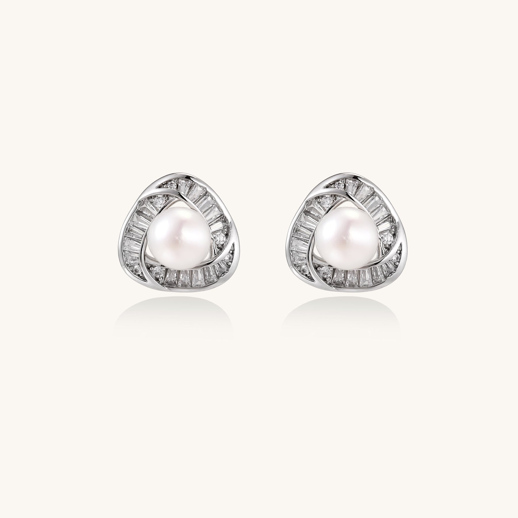 Close-up of triangular gold-plated stud earrings with central freshwater pearl surrounded by baguette crystals