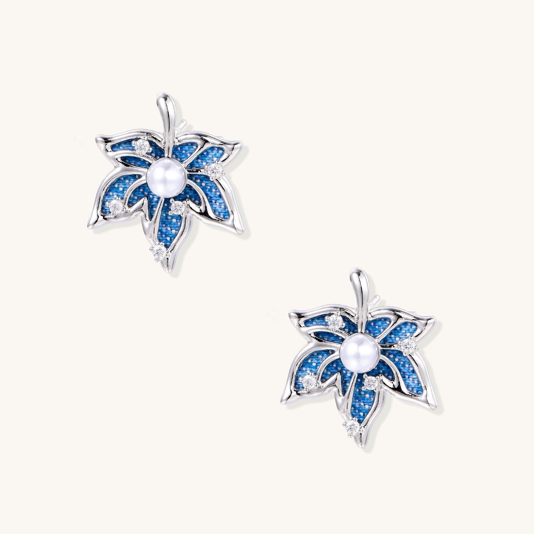 Silver-toned floral earrings with blue denim fabric petals, white pearls, and crystal accents on cream background.