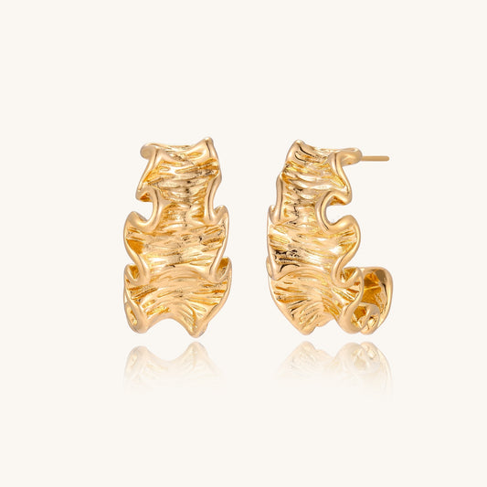 Close-up of dimensional gold-plated hoop earrings with rippled wave texture against white background.