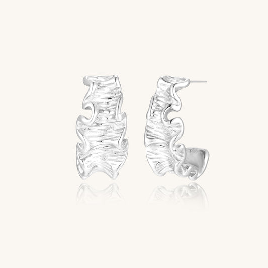 Textured gold-plated hoop earrings with flowing ripple design displayed on clean white background.