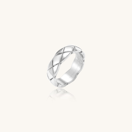 Close-up of a polished stainless steel ring featuring a geometric quilted diamond pattern on white background.