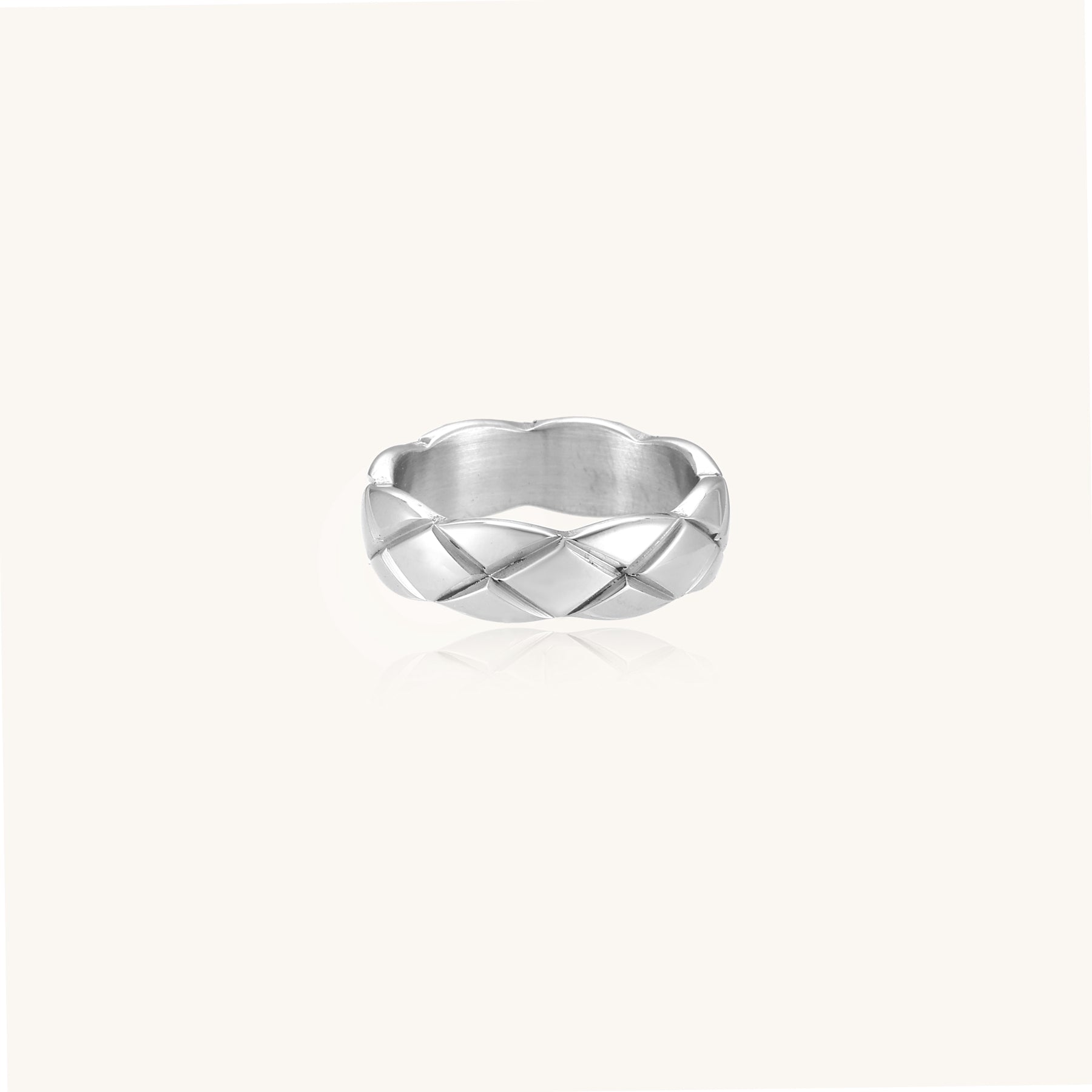 Close-up of a polished stainless steel ring featuring a geometric quilted diamond pattern on white background.
