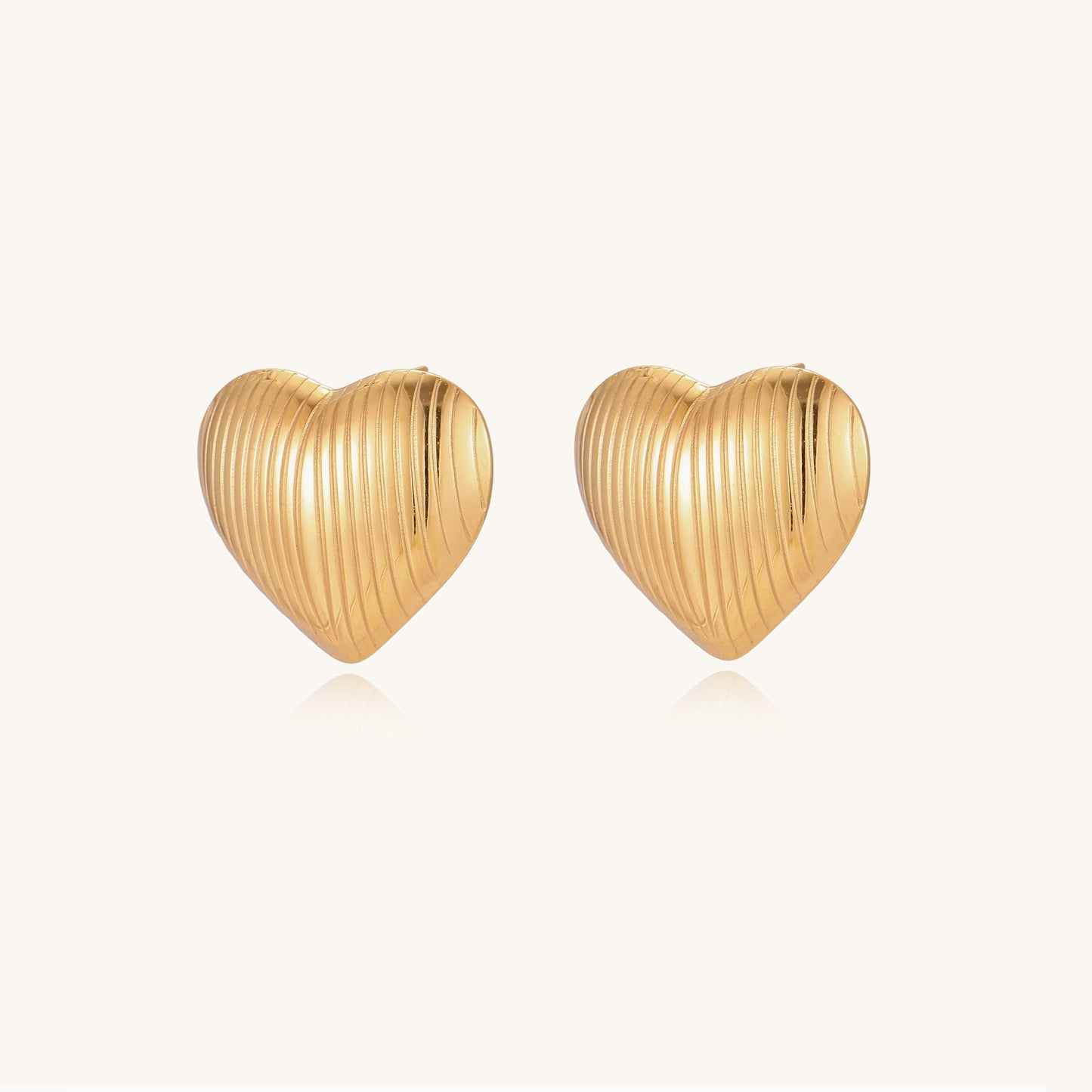 Close-up of ridged heart-shaped gold-plated stud earrings with textured surface pattern on cream background.