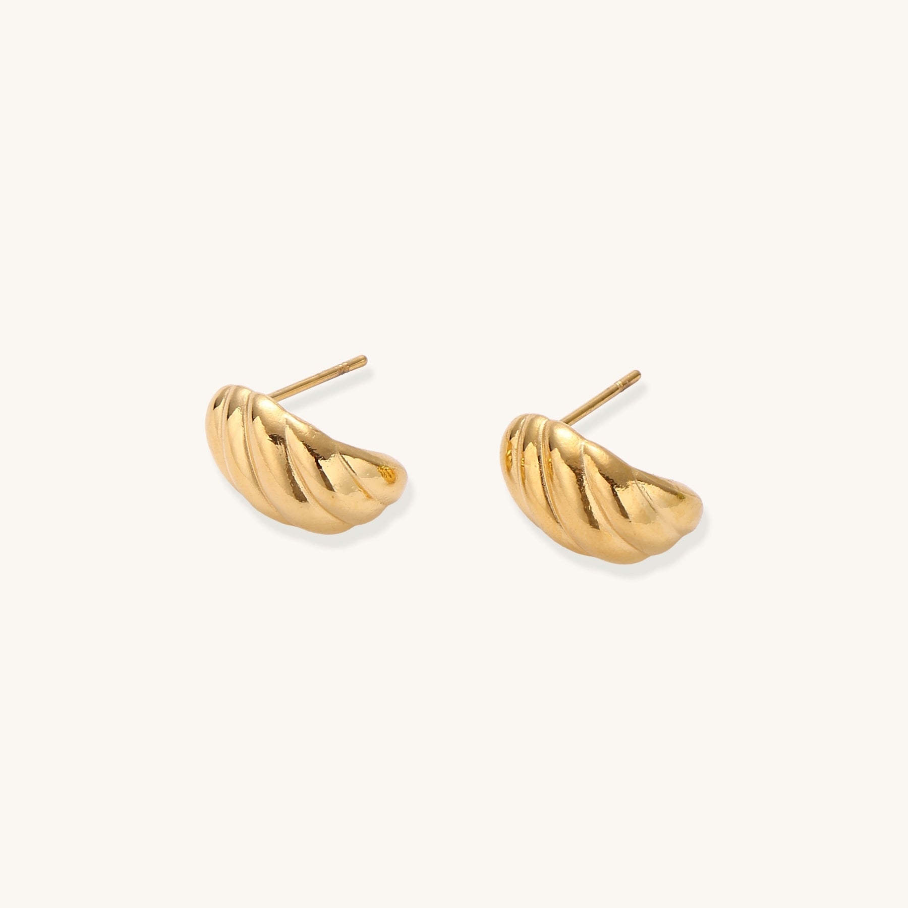 Pair of gold-plated twisted stud earrings with sculptural spiral design displaying elegant curved ridges on cream background.