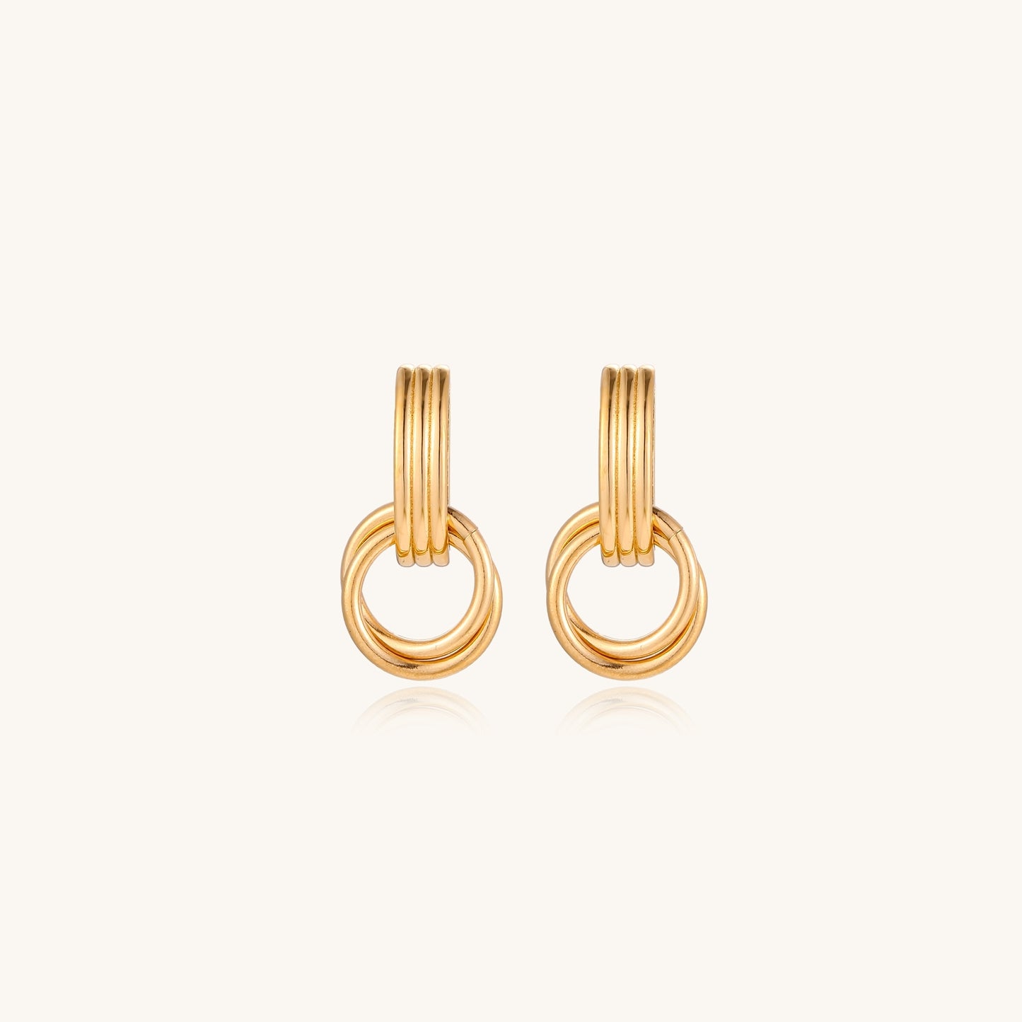Geometric gold earrings with ribbed linear top section and circular drop elements on white background.