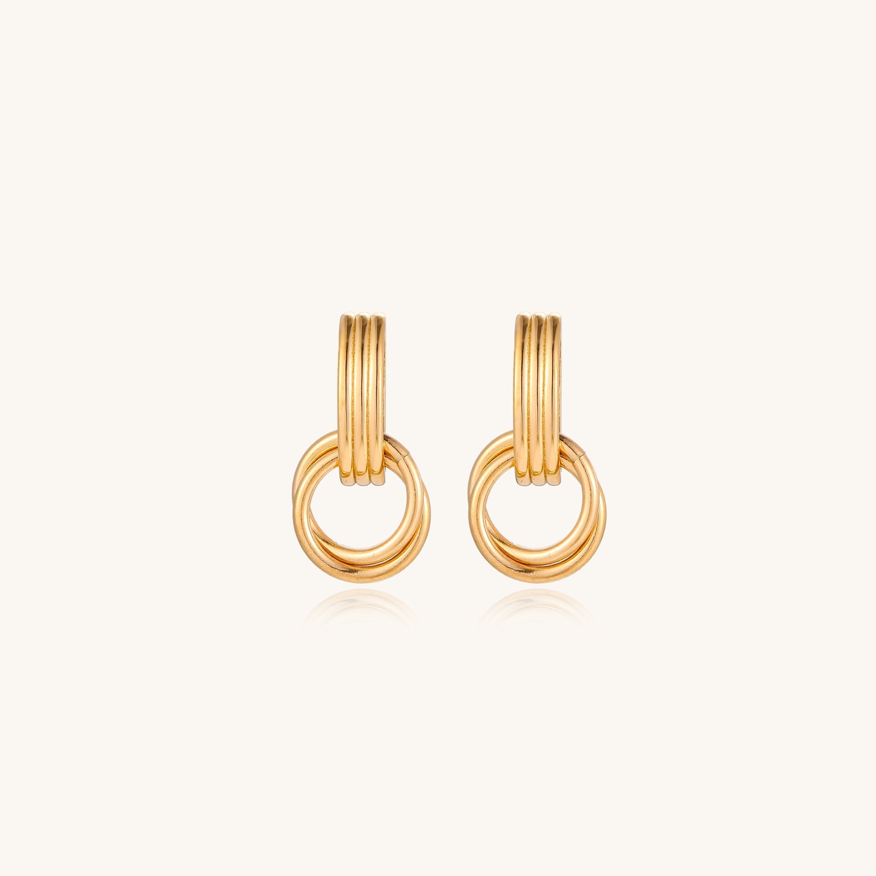 Geometric gold earrings with ribbed linear top section and circular drop elements on white background.