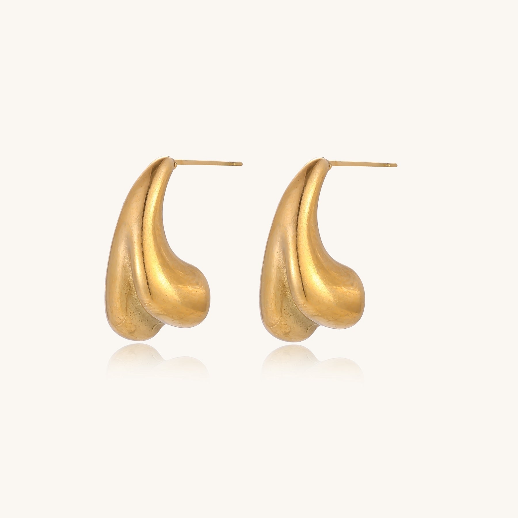 Pair of gold-plated sculptural stud earrings with organic teardrop shapes on neutral background.