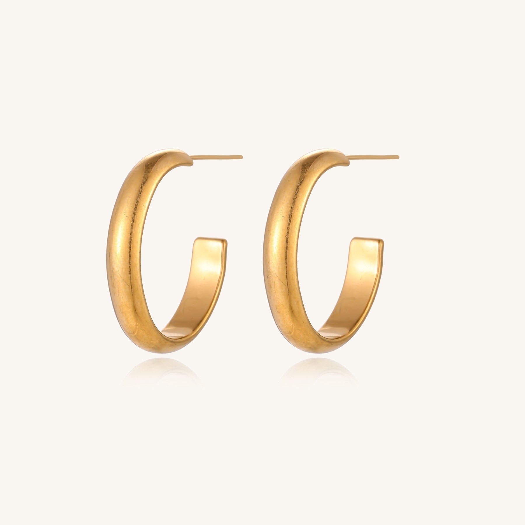 Four pairs of gold-plated stainless steel earrings including hoops and studs displayed on cream background