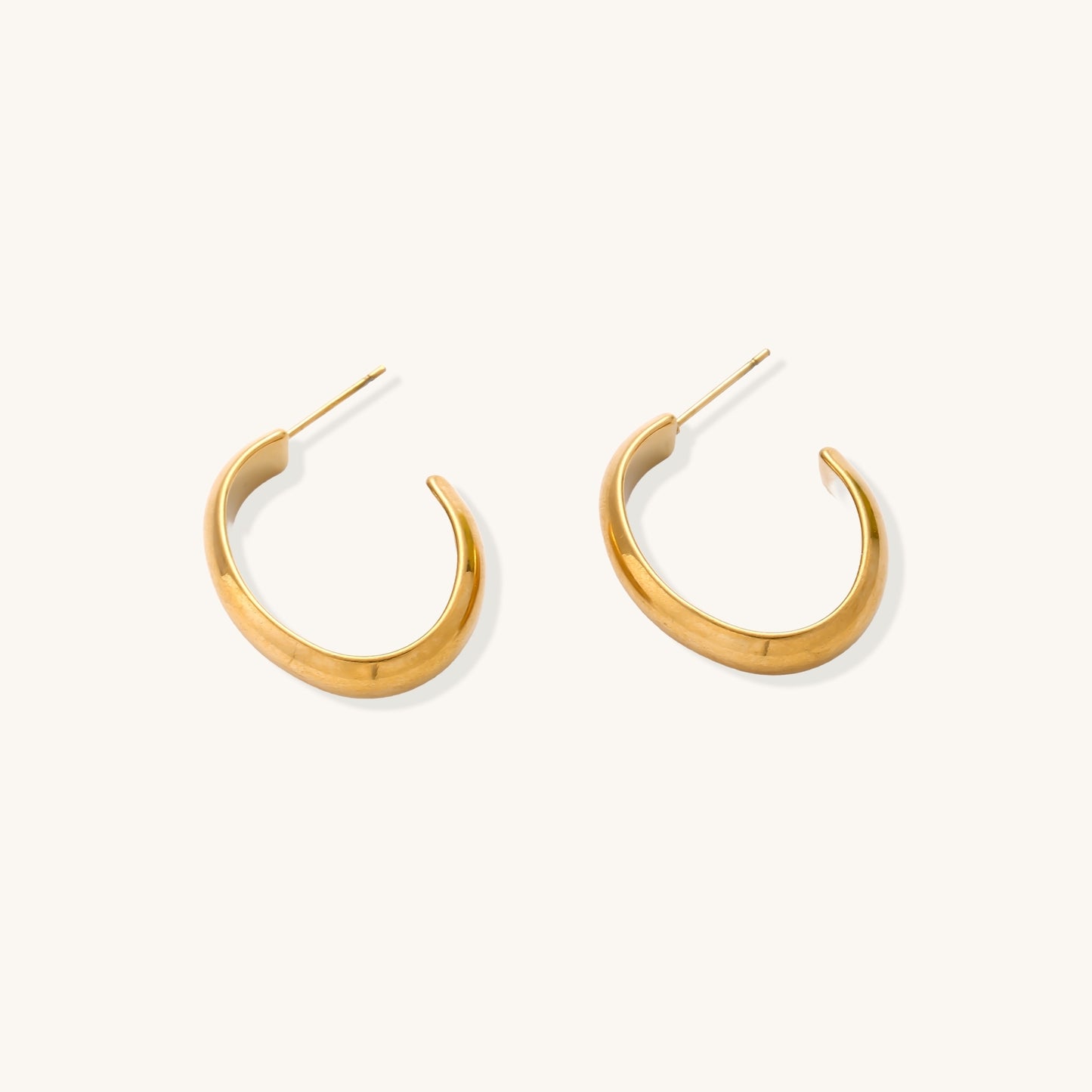 Four pairs of gold-plated stainless steel earrings including hoops and studs displayed on cream background