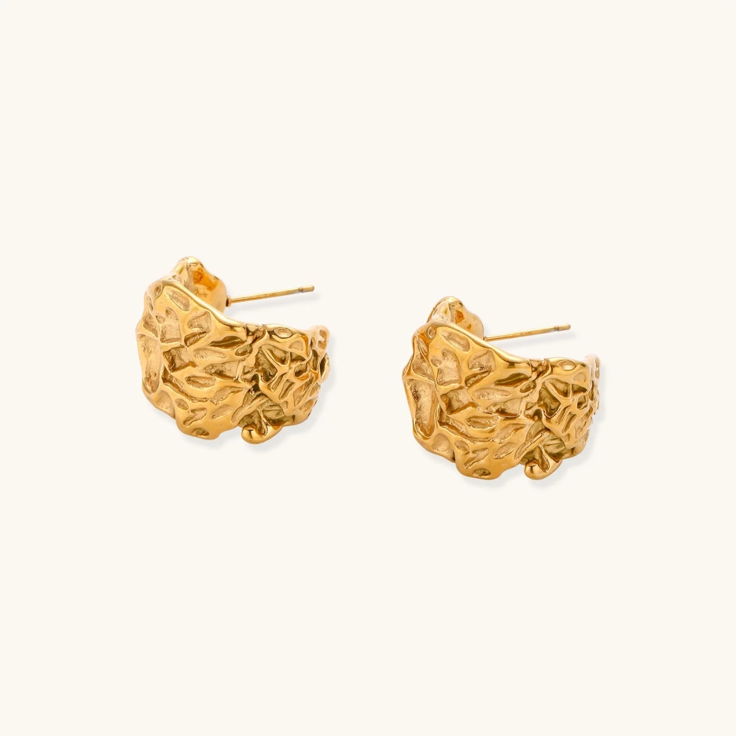 Textured gold-plated hoop earrings with organic molten surface pattern on cream background, showing intricate flowing details.